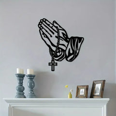 Black rosary and praying hands silhouette on a gray wall over a shelf