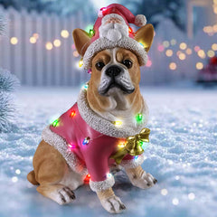 French bulldog Christmas statue in the snow with tree lights behind, its pink coat the only warm color in the shot