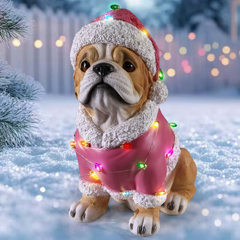 The Pug in the pink Santa coat standing on snow with a fence and house lights behind