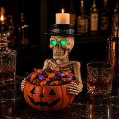 Skeleton figurine holding an orange pumpkin candy bowl filled with chocolates, with a lighted candle standing in its top hat