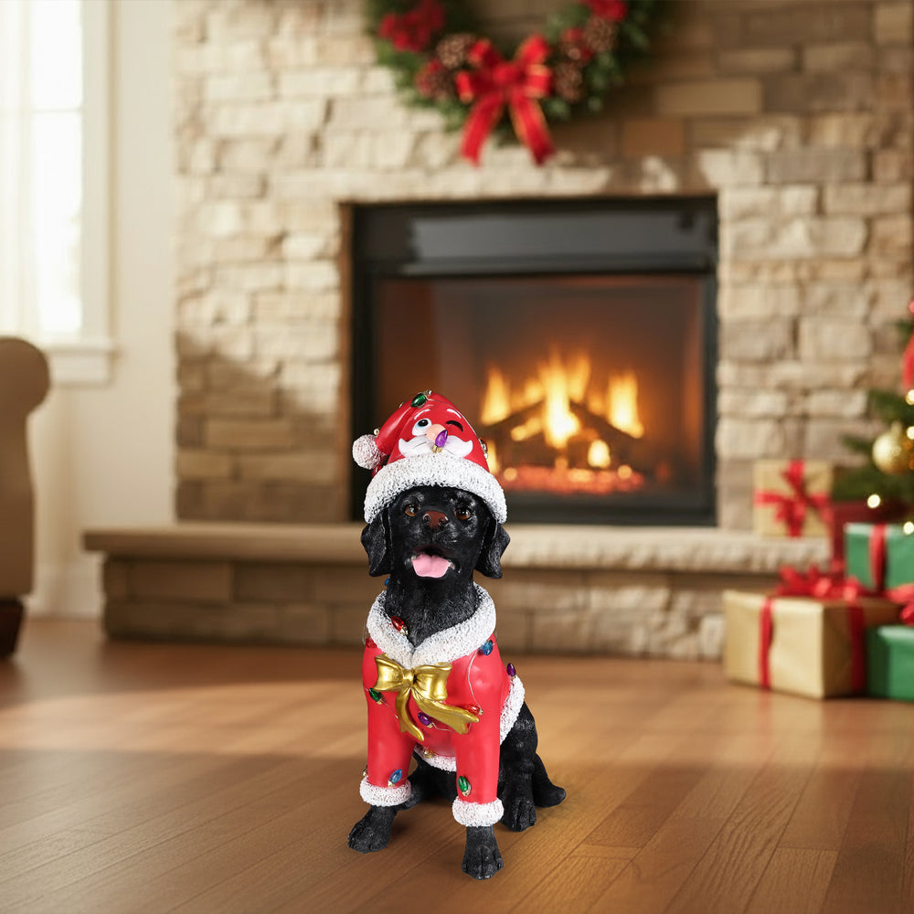 The Black labrador retriever in the red Santa coat sitting on the floor in front of a lit fireplace