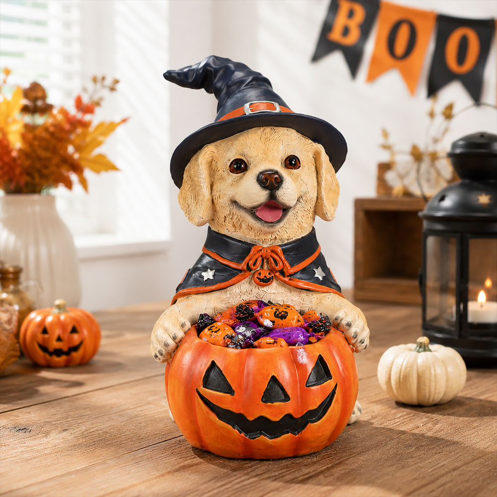 Yellow labrador puppy in a witch hat sitting behind a carved pumpkin bowl filled with candy on a decorated table