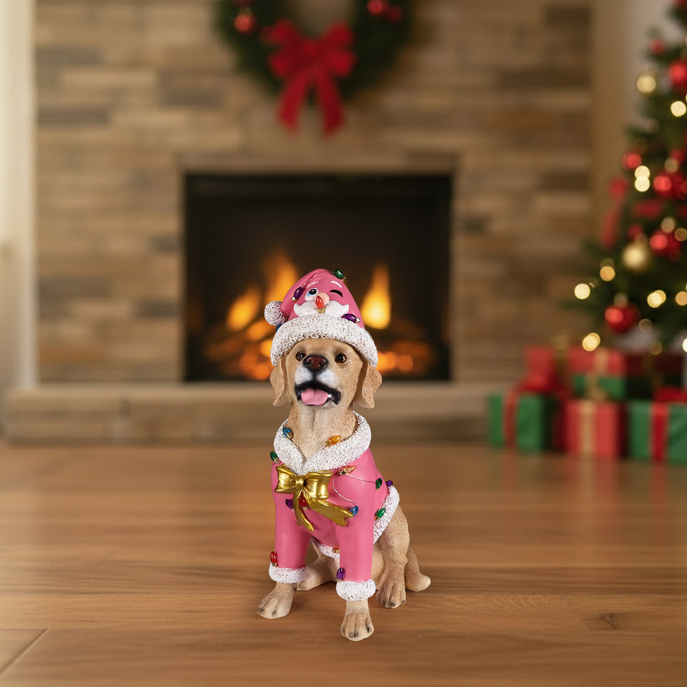 The Labrador retriever in the pink Santa coat sitting on the floor in front of a lit fireplace
