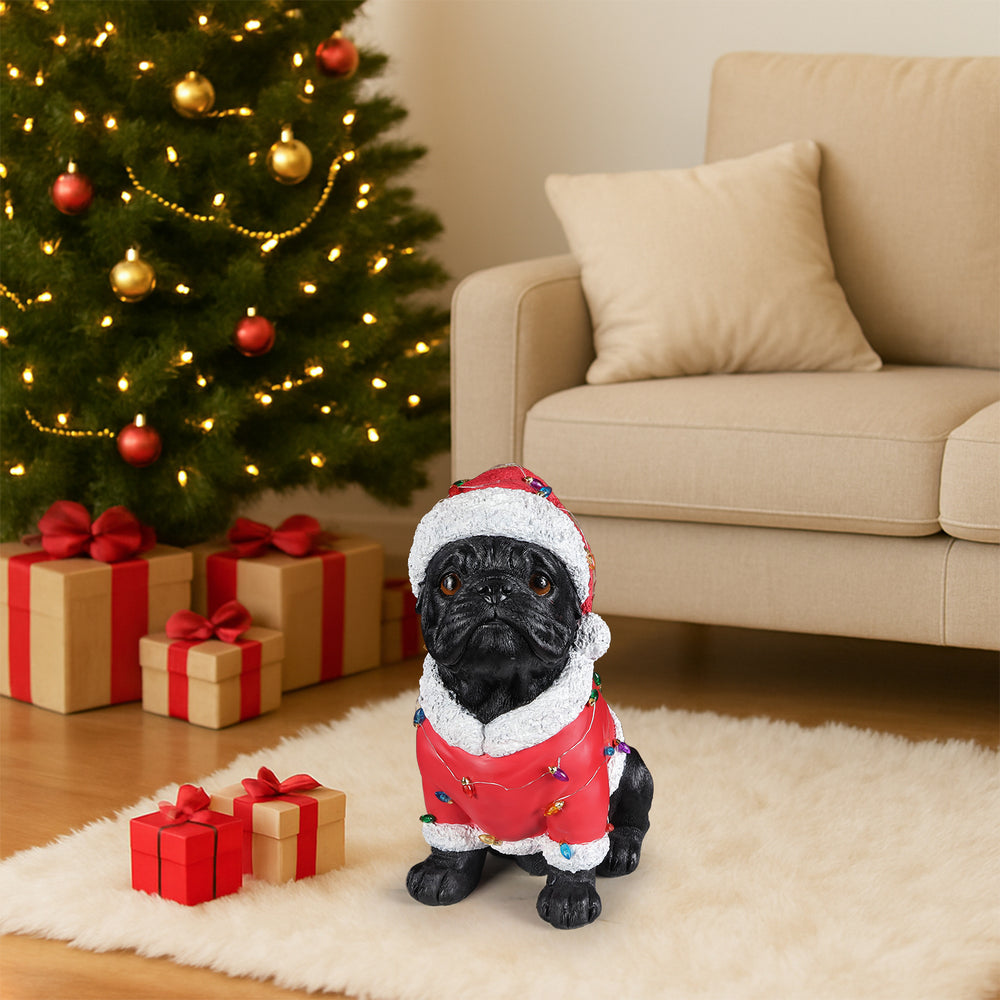 The Pug in the red Santa coat set on the floor beside a lit Christmas tree with gifts under it