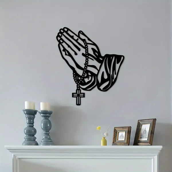 Black rosary and praying hands silhouette on a gray wall over a shelf