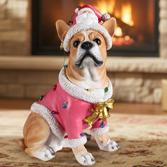 Cream French bulldog with a white marked muzzle in a pink Santa coat and hat, sitting in front of a lit fireplace