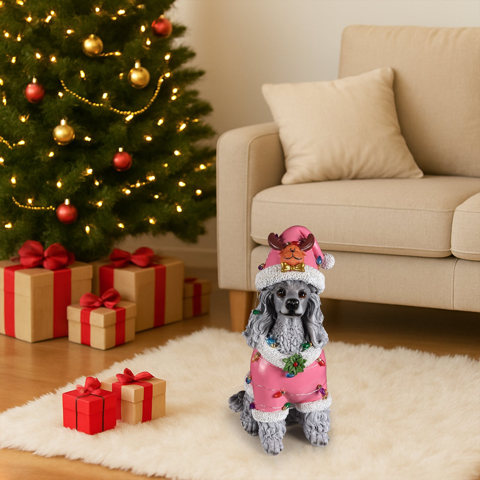 The Poodle in the pink Santa coat set on the floor beside a lit Christmas tree with gifts under it