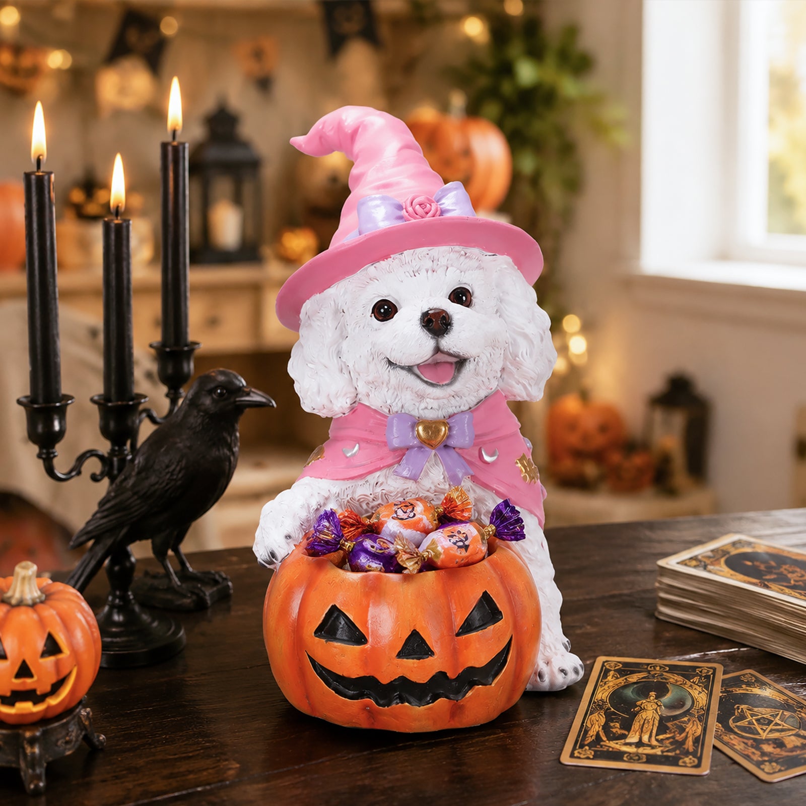 White curly coated puppy in a pink witch hat holding a pumpkin candy bowl on a table with candles and tarot cards