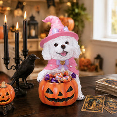 White curly coated puppy in a pink witch hat holding a pumpkin candy bowl on a table with candles and tarot cards