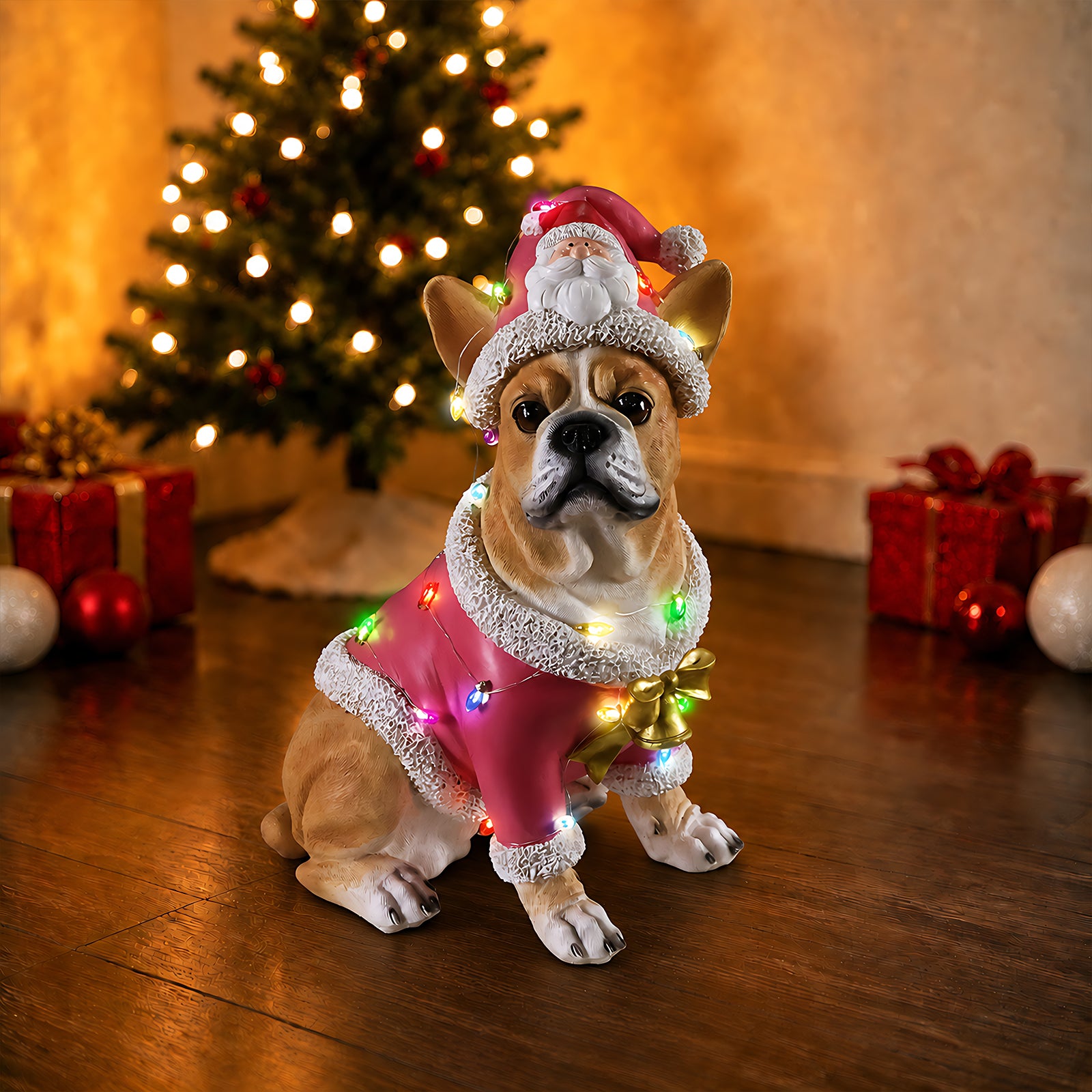 The same cream French bulldog Christmas statue beside a lit tree with wrapped gifts
