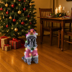 The Poodle in the pink Santa coat on a hard floor by a Christmas table with candles lit