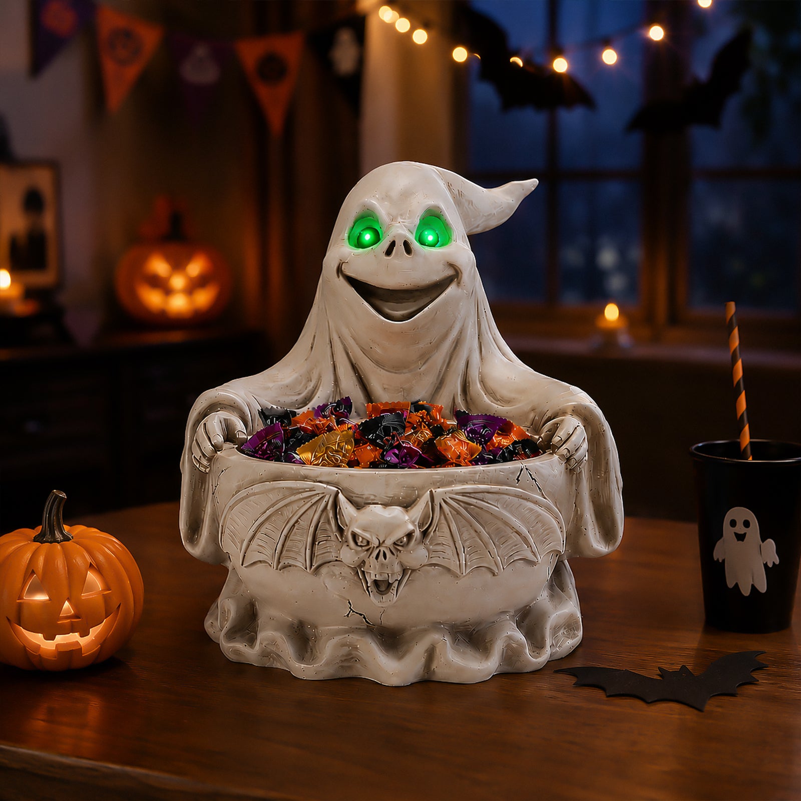 Ghost candy bowl figurine holding a wide bat wing dish filled with chocolates, on a table with pumpkins and string lights