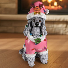 A gray poodle sitting in a pink Santa coat with a string of colored lights across the back, a reindeer Santa hat on the head, in a living room at Christmas