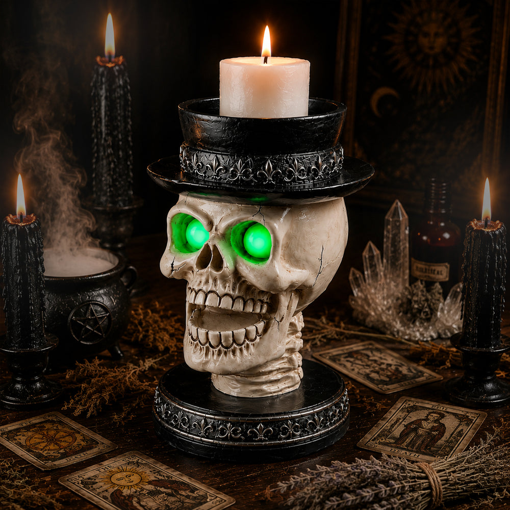 Gothic skull candle holder with a lighted pillar candle in the flat top hat, on a dark table beside cards and a pumpkin
