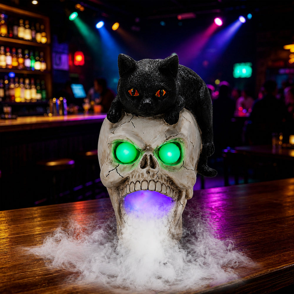Black cat skull fogger statue on a bar counter at night with a black cat crouched over a glowing skull and mist on the surface