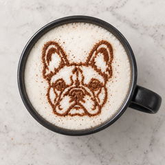 Overhead view of a French bulldog face dusted in cocoa powder on the foam of a coffee in a black mug