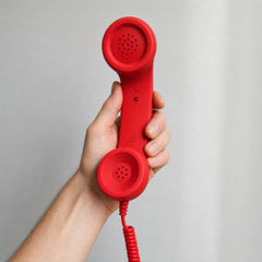 Retro smartphone handset in red, held in the hand with the coiled cord running down